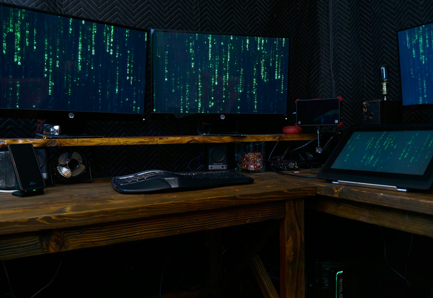 Wiele monitorów komputerowych wyświetlających zielony kod w ciemnym pomieszczeniu.